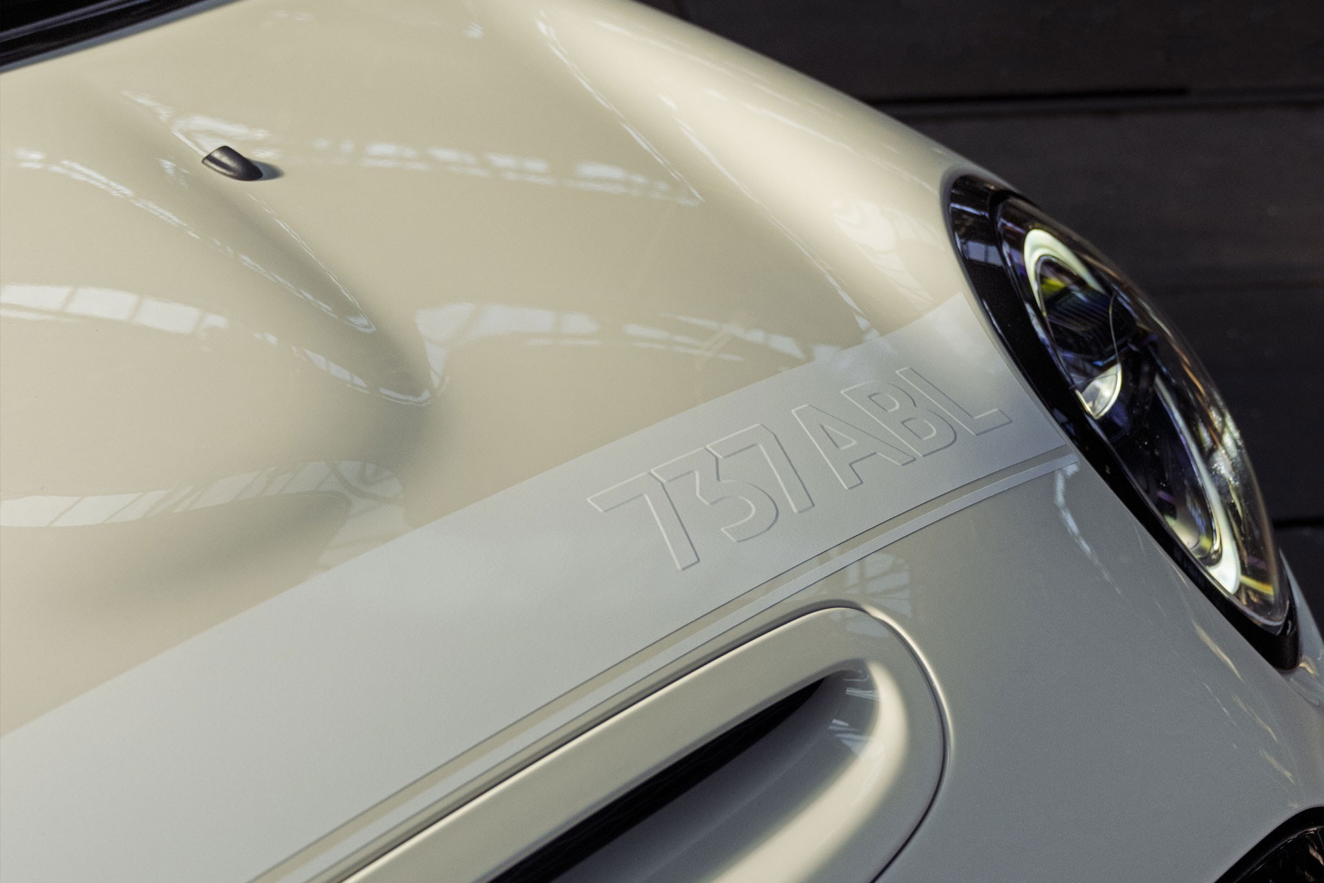 Close-up of a white bonnet with a horizontal stripe and the plate number, 737 ABL, that shimmers with a cool 3D effect. 